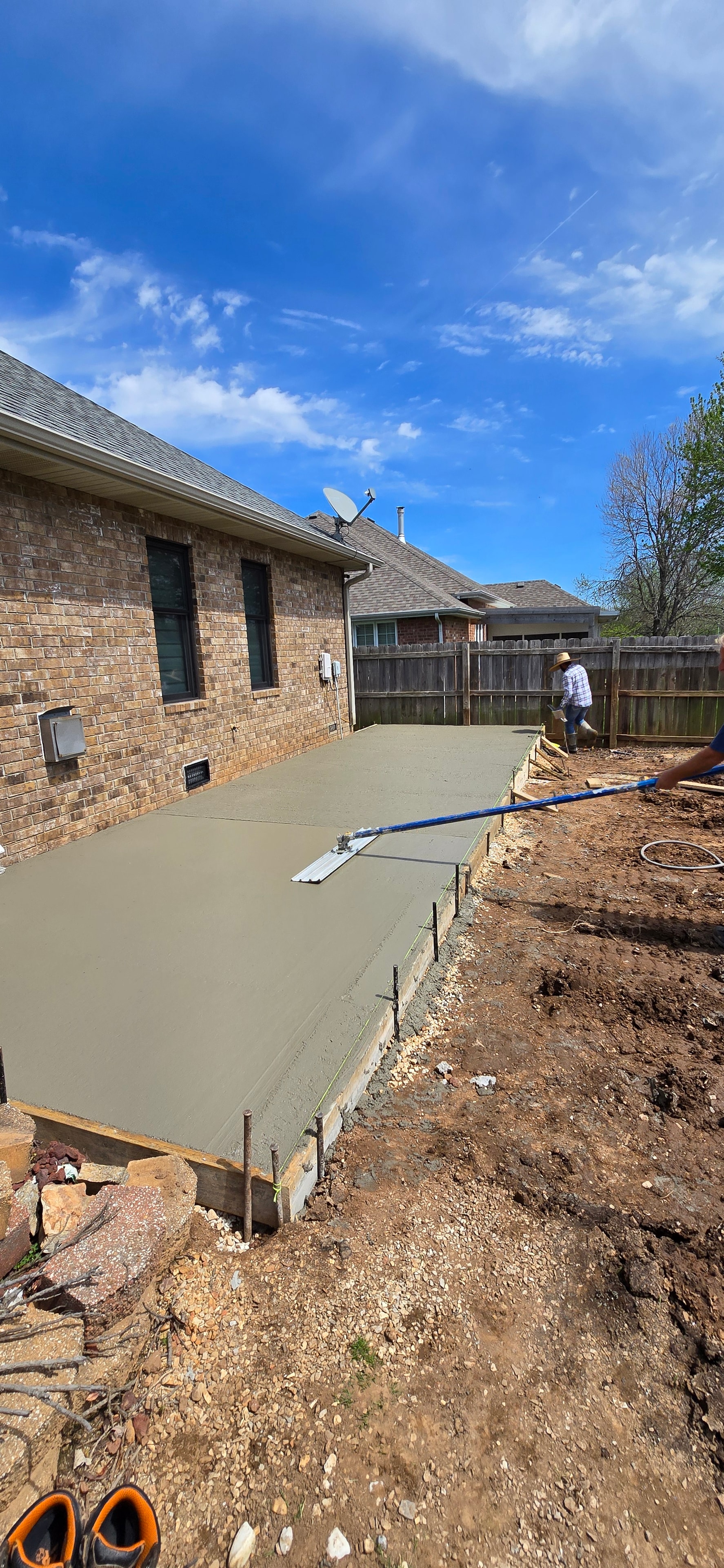 Freshly poured residential concrete patio beside a brick home